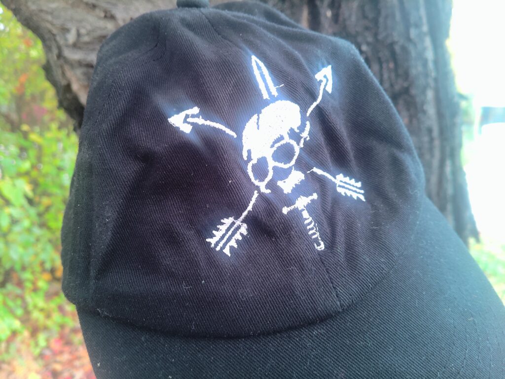 Depiction of a black cap with sword and arrows piercing a skull